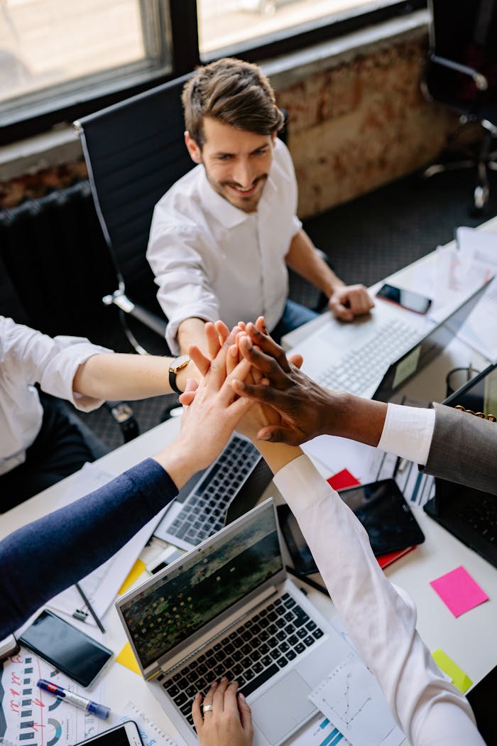 Group of diverse colleagues joining hands around a desk, symbolizing teamwork and unity.